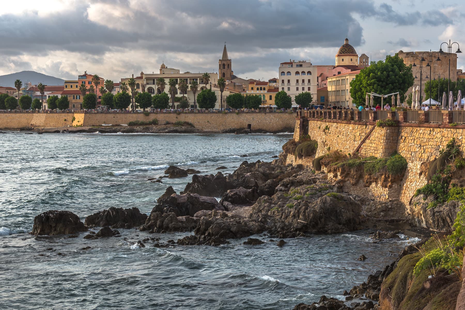 The sandstone sea bastions of Alghero at dusk, the old town skyline behind them