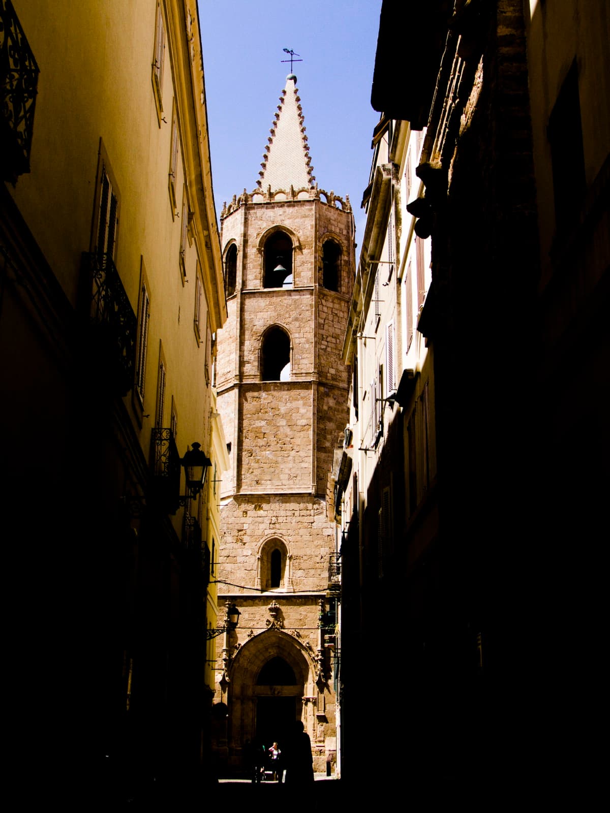 Bell tower of Santa Maria cathedral rising over a narrow lane in Alghero's old town