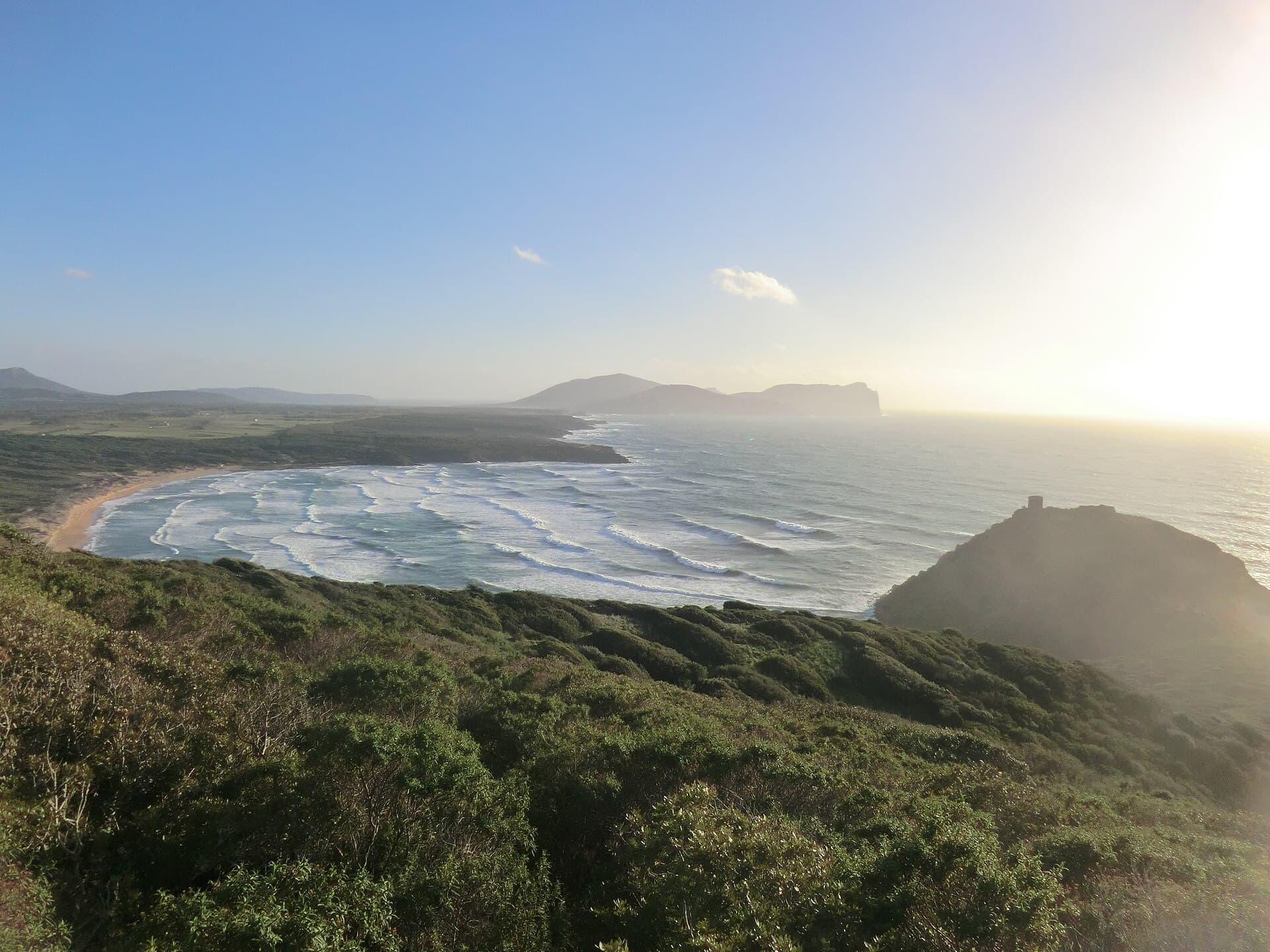 Rolling surf in the wide bay of Porto Ferro with a watchtower on the headland